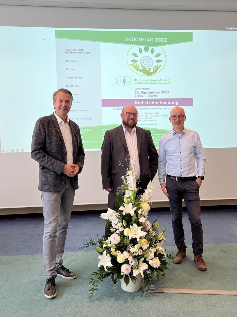 Eröffnung des Aktionstages. Drei Männer stehen vor einer Präsentationswand.